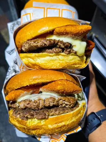 Dois King Gouda empilhados na mão, com o gouda empanado aparecendo entre o brioche e a carne